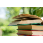 A stack of books in front of a wooded landscape on a sunny day