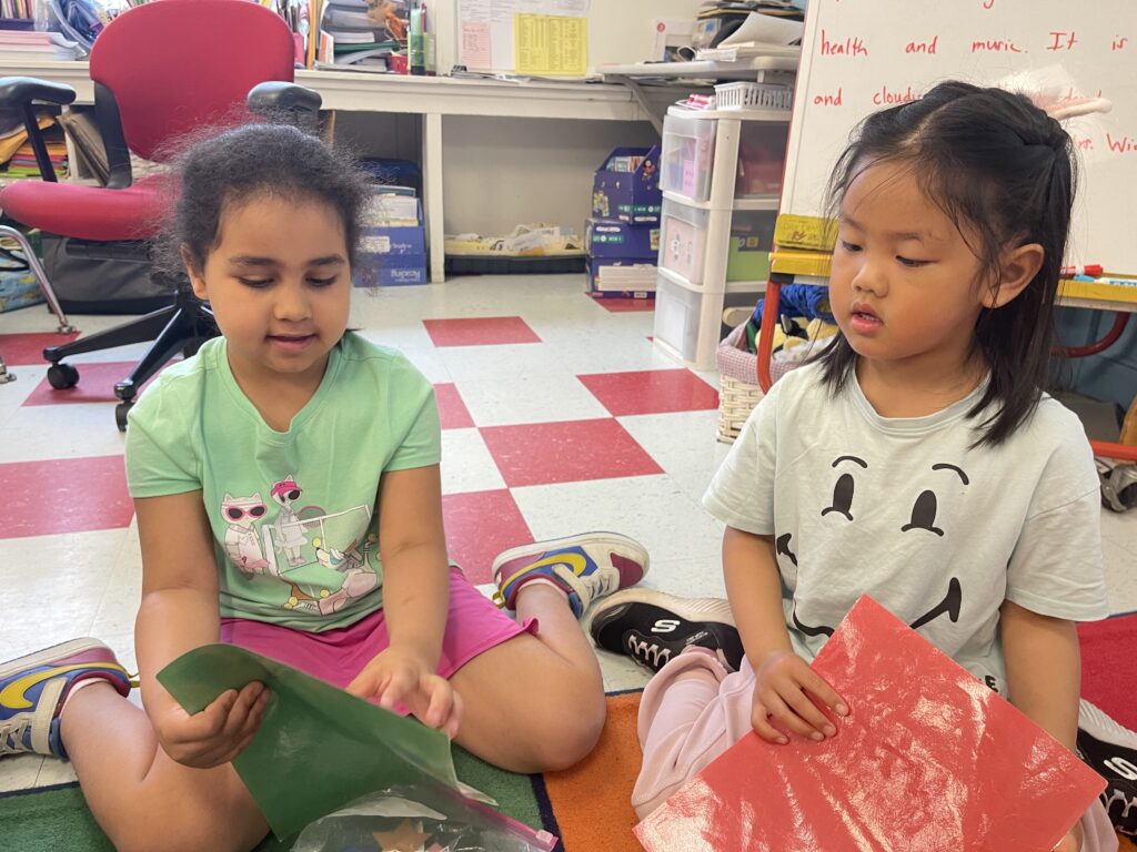 Two students sitting on a colorful classroom floor learning about shapes