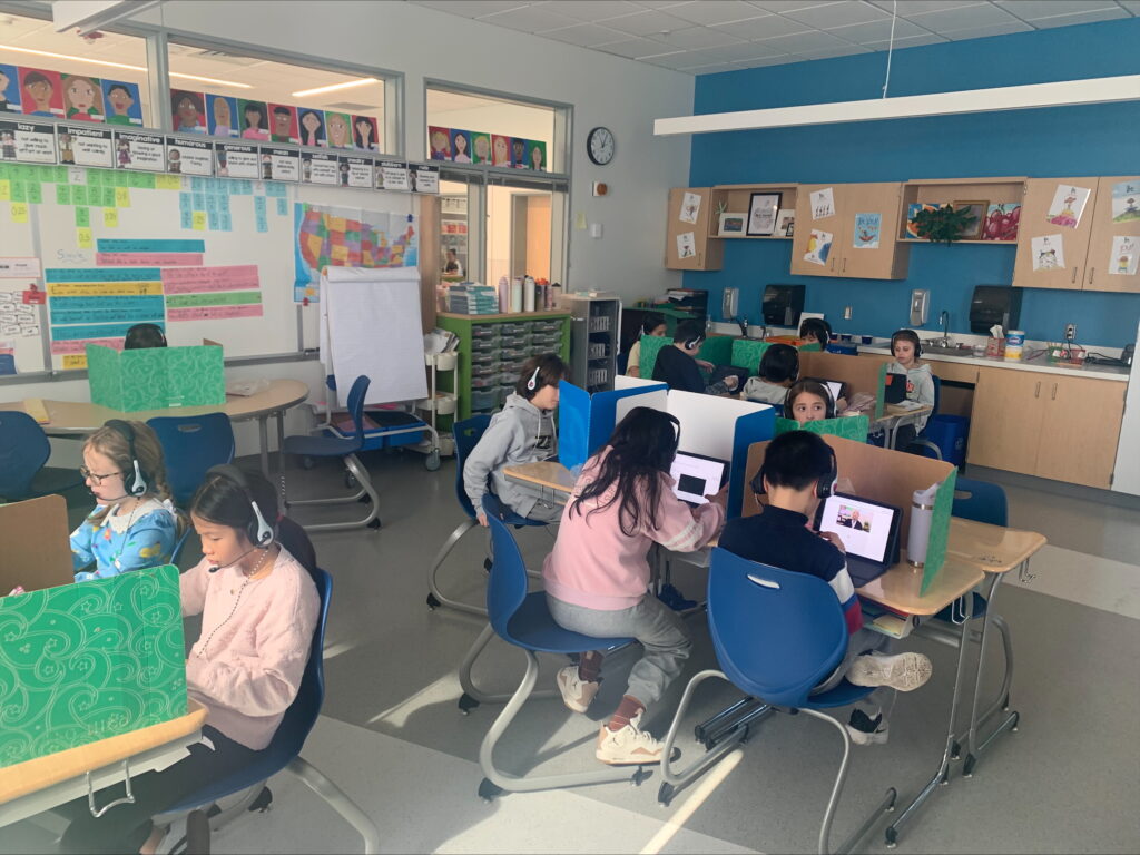 Students at desks in the classroom using headphones, mics and iPads to practice listening and speaking