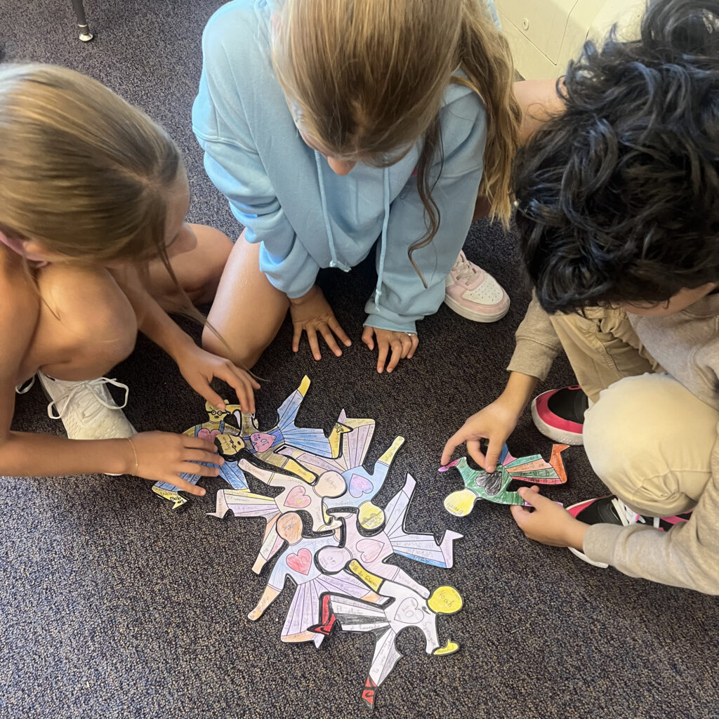 Three students on a rug putting a puzzle together made up of colored paper figures
