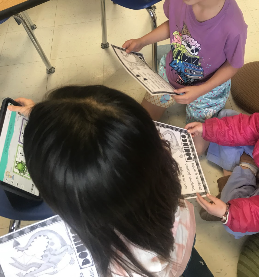 Three students working on an assignment about a dragon on an iPad and on paper
