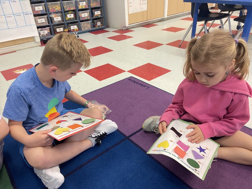 Two students sitting on a colorful classroom floor learning about shapes