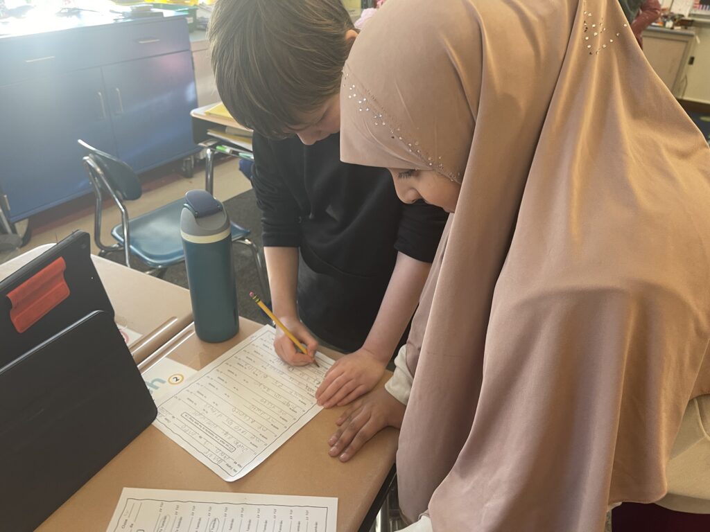 Two students standing at a desk together writing on worksheets