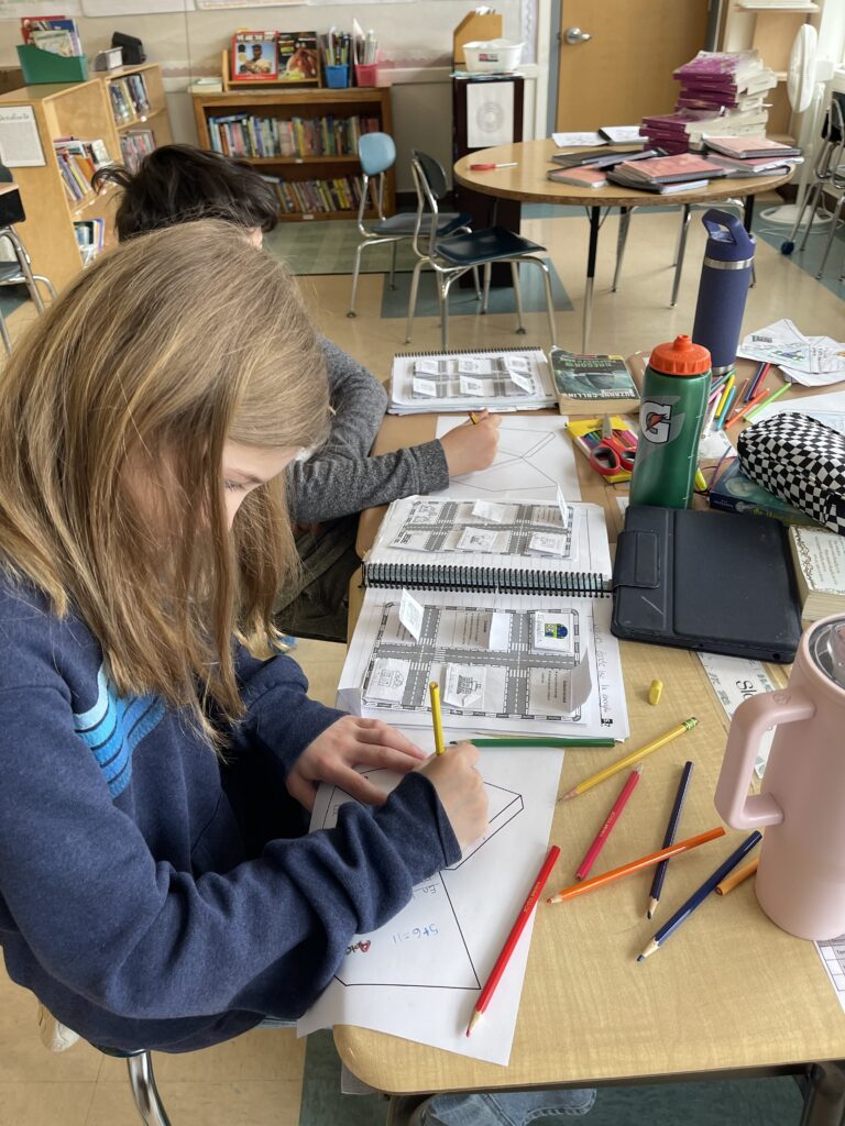 Two students working at their desk on paper with colored pencils