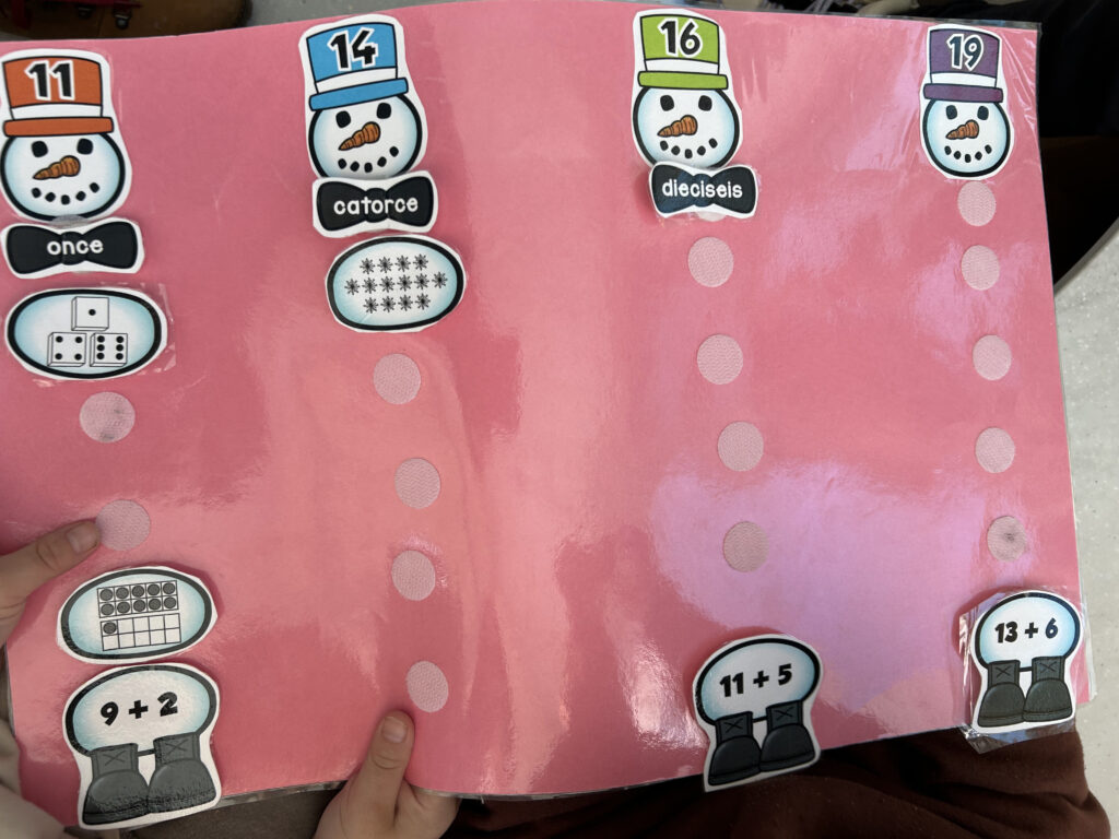 A pink sheet of paper with snowmen being built out of numbers in different formats labeled in Spanish
